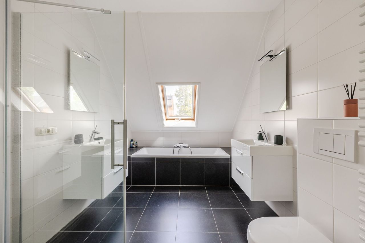 De badkamer met ligbad, dubbele wastafel en dakraam