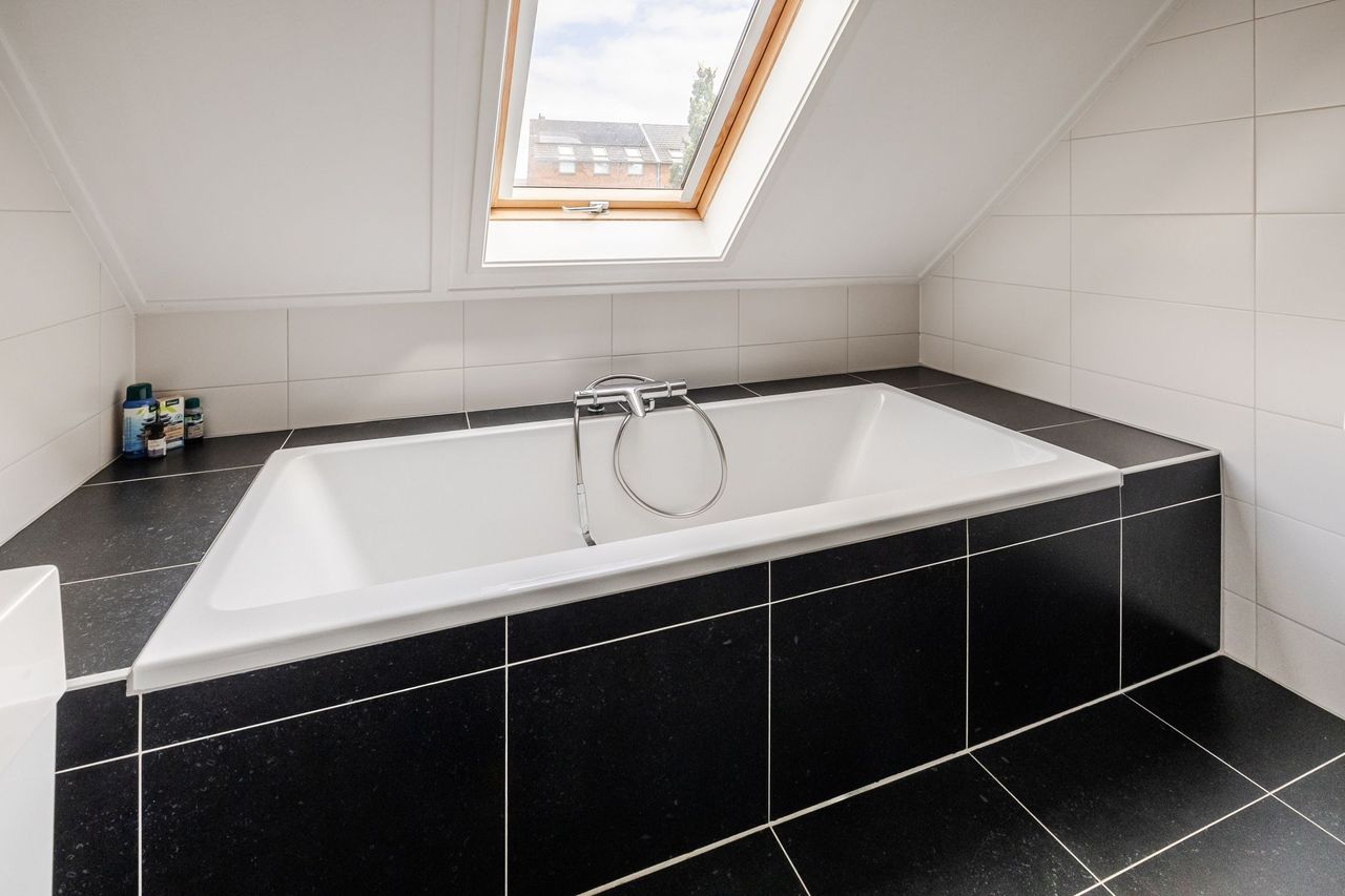 Het ligbad onder het dakraam, met zwarte tegelvloer