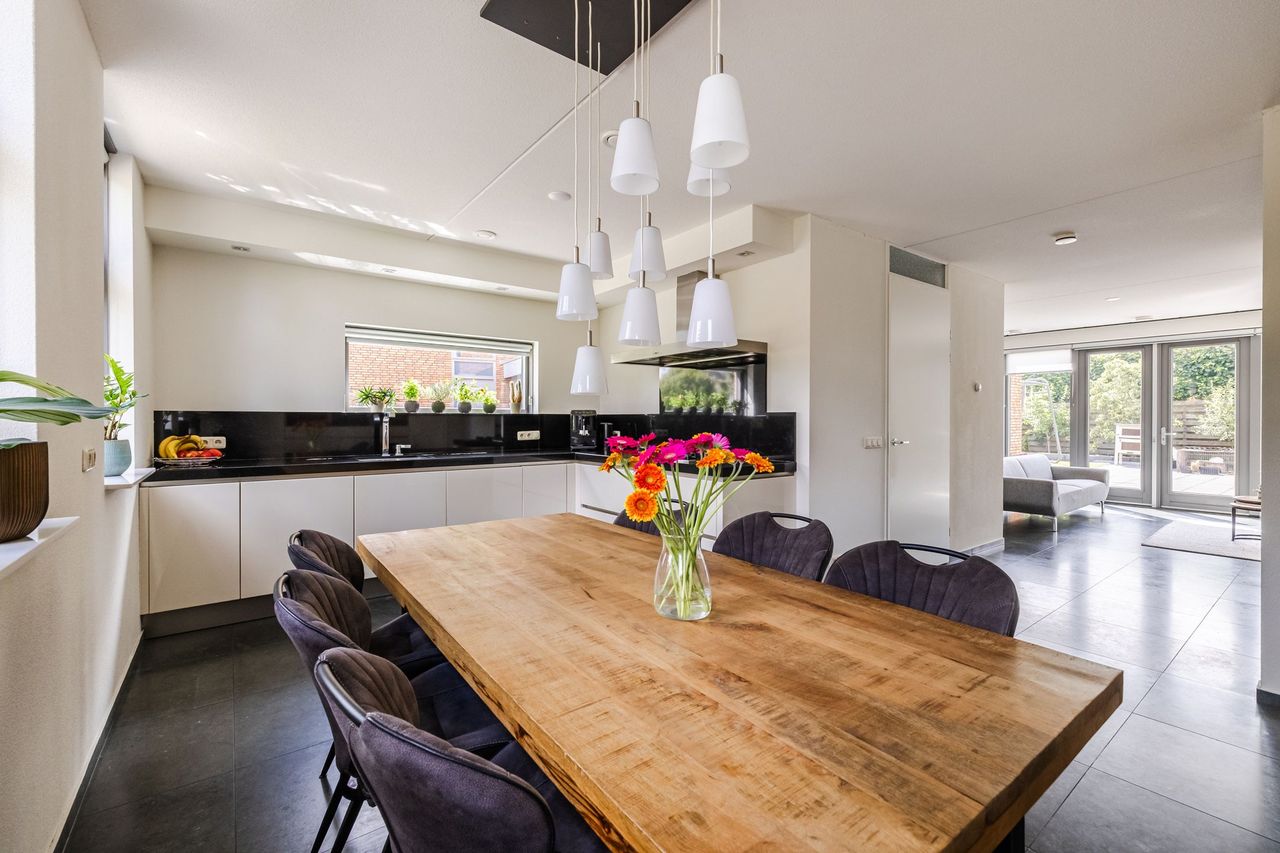 De keuken met de grote houten eettafel ervoor en doorkijk naar de woonkamer