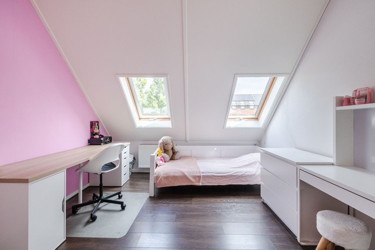 Zolderkamer met bed, bureau en twee dakramen