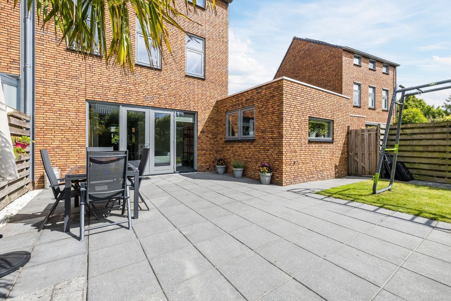Het terras aan de openslaande deuren, met tuinmeubels onder de palm en gazon ernaast