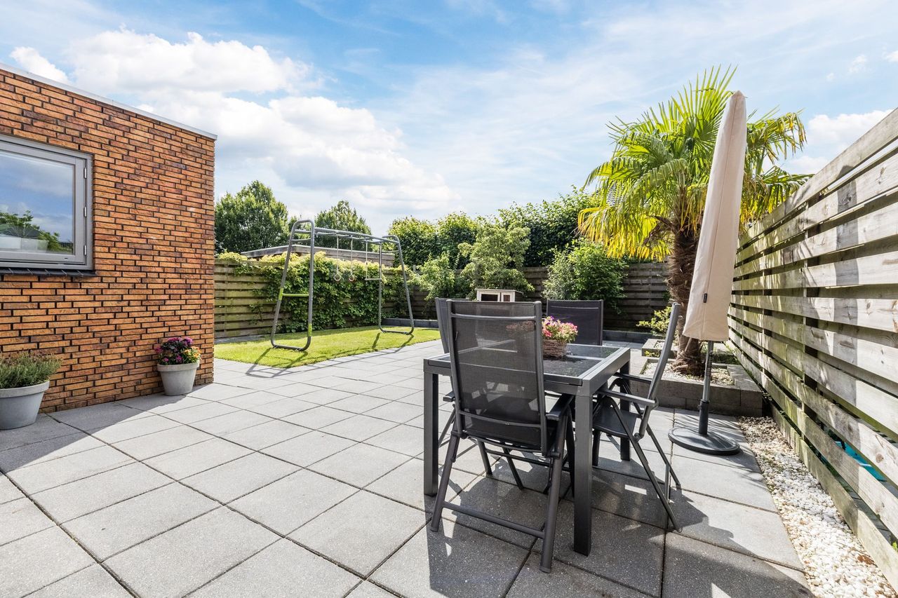 Het terras in de achtertuin met eettafel, parasol en een palm