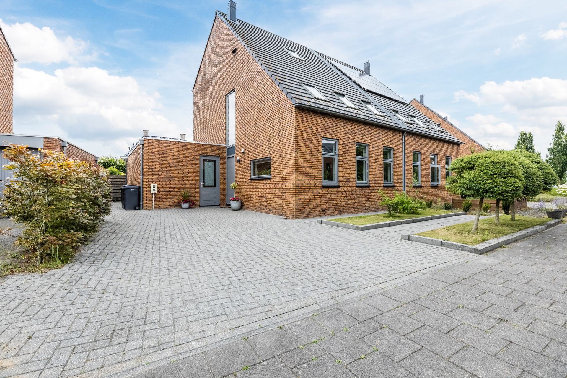 De voorgevel van Bosrank 55 in Assen, een twee-onder-een-kapwoning met ruime oprit onder een blauwe zomerlucht